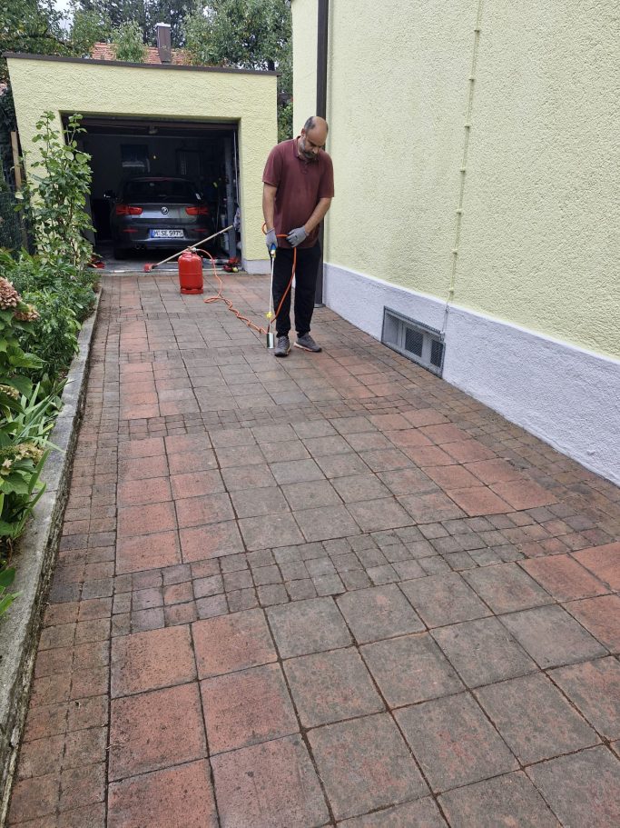 Gepflegter Weg am Haus Mann fegt einen gereinigten Pflasterweg neben einer Hauswand und einer Garage.